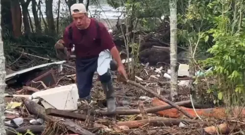 ▲紅衣大哥將狗狗捧在手上，跨越馬太鞍溪堰塞湖洪水帶來的漂流物。（圖／Threads@karo_tafed）