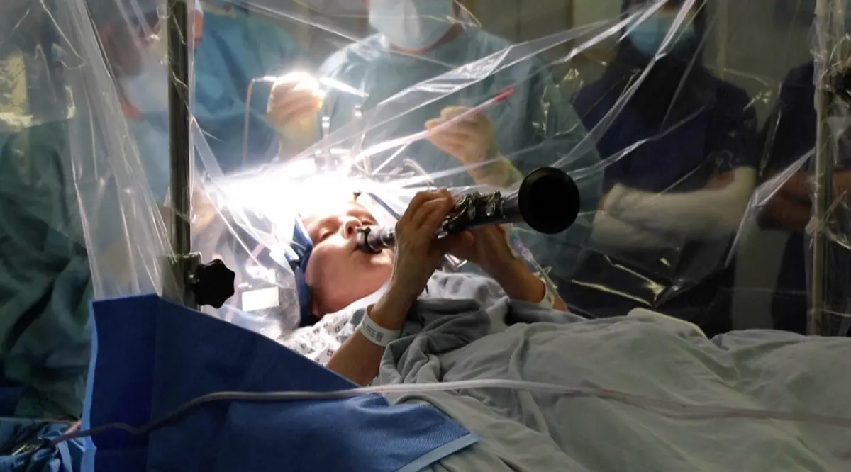▲英國一名罹患帕金森氏症的婦女，近日在接受腦部手術時，一邊開刀一邊在手術台上吹奏起單簧管，以讓現場醫護人員可以即時監控手術狀況。（圖／翻攝自美聯社via@倫敦國王學院附設醫院影片截圖）