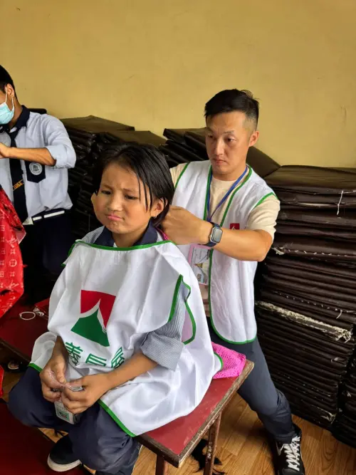 ▲滿頭蟲卵的尼泊爾女孩因被醫生團評估頭髮需剪短才能免除頭蝨困擾面露不捨，信義房屋吳正義在當地協助孩子修髮。（圖／信義房屋）