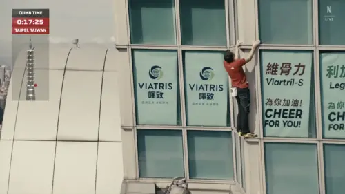 ▲霍諾德攀爬台北101約17分鐘時，直播畫面竟看見101窗內有多個廣告，其中維骨力超級顯眼。（圖／翻攝自Netflix）