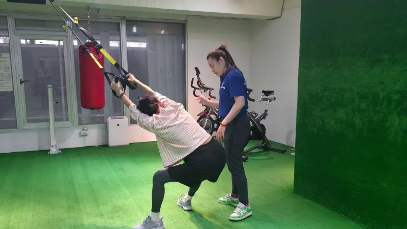 ▲教練透過懸吊輔助訓練，引導長者在可控制的強度下進行深蹲與下肢穩定訓練，降低膝關節負擔，同時強化臀腿肌力與平衡感。（圖／翻攝畫面）