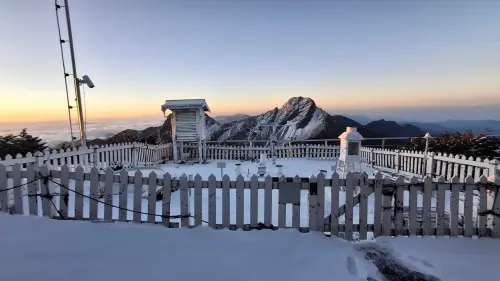 ▲晨曦中的玉山氣象站： 圍欄與氣象觀測儀器在薄雪中佇立，後方山頭與清晨的天光交織出靜謐氛圍。（圖／中央氣象署提供）