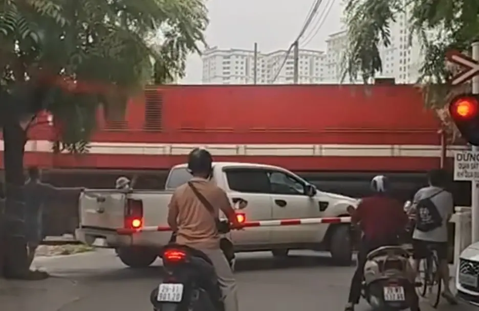 ▲轎車卡在越南河內平交道鐵軌上動彈不得，民眾一度上前協助脫困未果，隨後列車高速撞上車體，造成車輛嚴重毀損、道閘設施受損，現場畫面驚險。（圖／翻攝自勞動報）