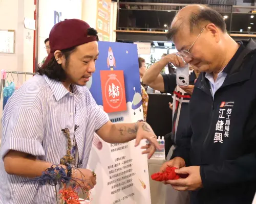 ▲高雄市政府勞工局局長江健興(右)在斜槓創業主題展活動中參觀勞工大學學員陳列展示的作品。(圖／高雄市政府勞工局提供)