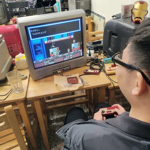 ▲玩家坐在懷舊的小學課桌椅前，手握紅白機經典手把對著 SONY 映像管電視破關，瞬間重回童年精神時光屋。（圖／翻攝自Google評論）