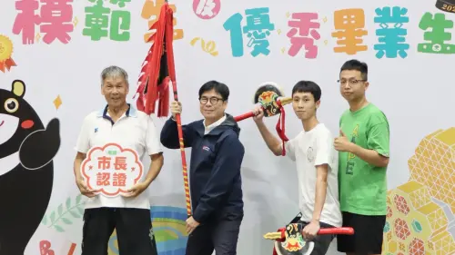 ▲岡山農工模範生暨市長獎畢業生何宇祐，今天與阿公、弟弟帶著象徵家族精神的宋江陣頭旗與雙斧，和市長陳其邁一同合影。（圖／高市府教育局提供）