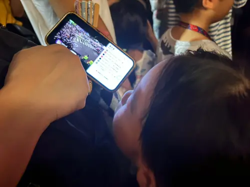 ▲因現場人潮太多、難以看見遊行隊伍，有家長直接打開手機直播，讓孩子透過螢幕看大象。（圖／記者林若瑋攝）