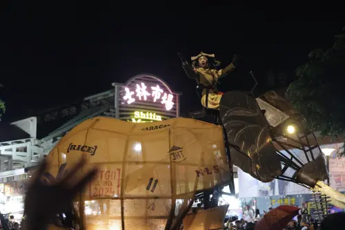 ▲巨型機械大象行經士林市場前方，演員站在象背上與沿途觀眾互動，熟悉街景瞬間化身大型戶外劇場。（圖／記者朱永強攝）
