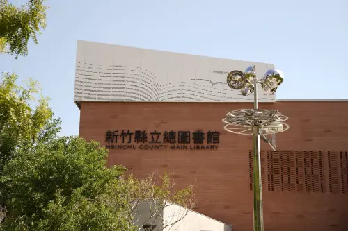 ▲新竹縣立總圖緊鄰東興圳公園，紅磚建築外觀搭配公共藝術動態風鈴雕塑。（圖／新竹縣政府提供）